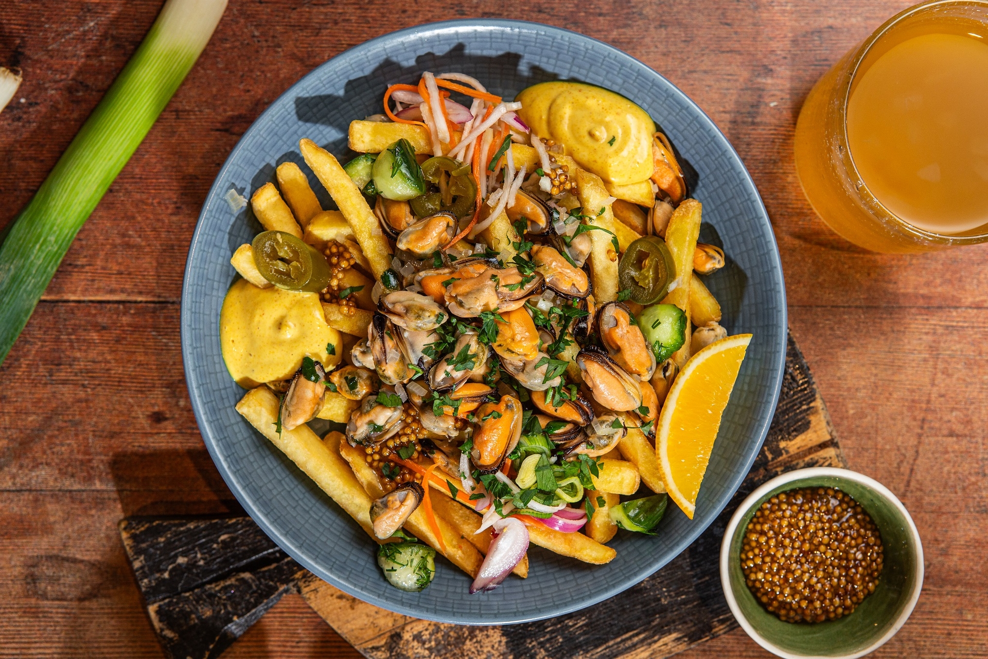 mule zaserwowane w restauracji w miseczce, z frytkami Aviko, sosem, warzywami, obok miseczka z musztardą francuską
