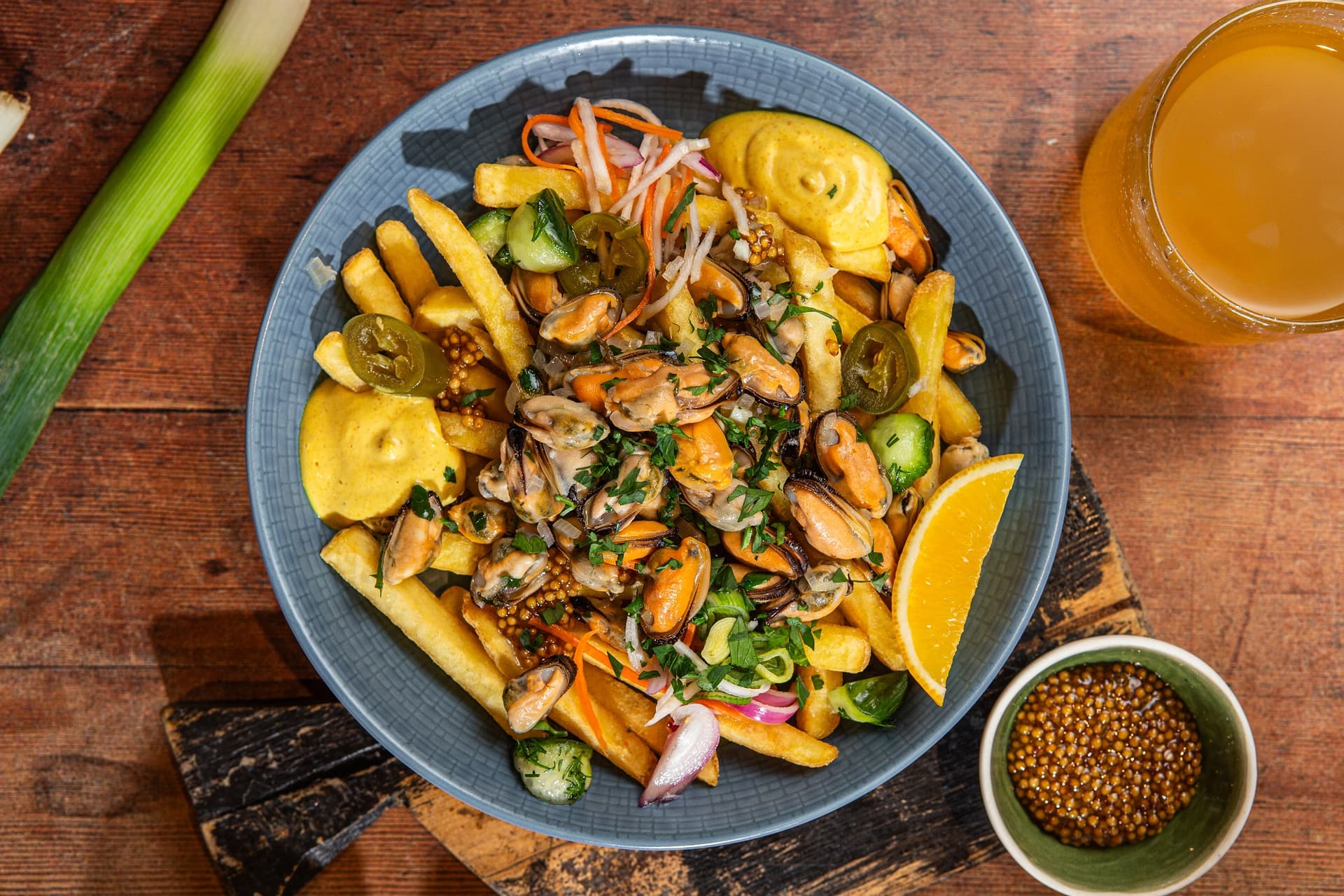mule zaserwowane w restauracji w miseczce, z frytkami Aviko, sosem, warzywami, obok miseczka z musztardą francuską