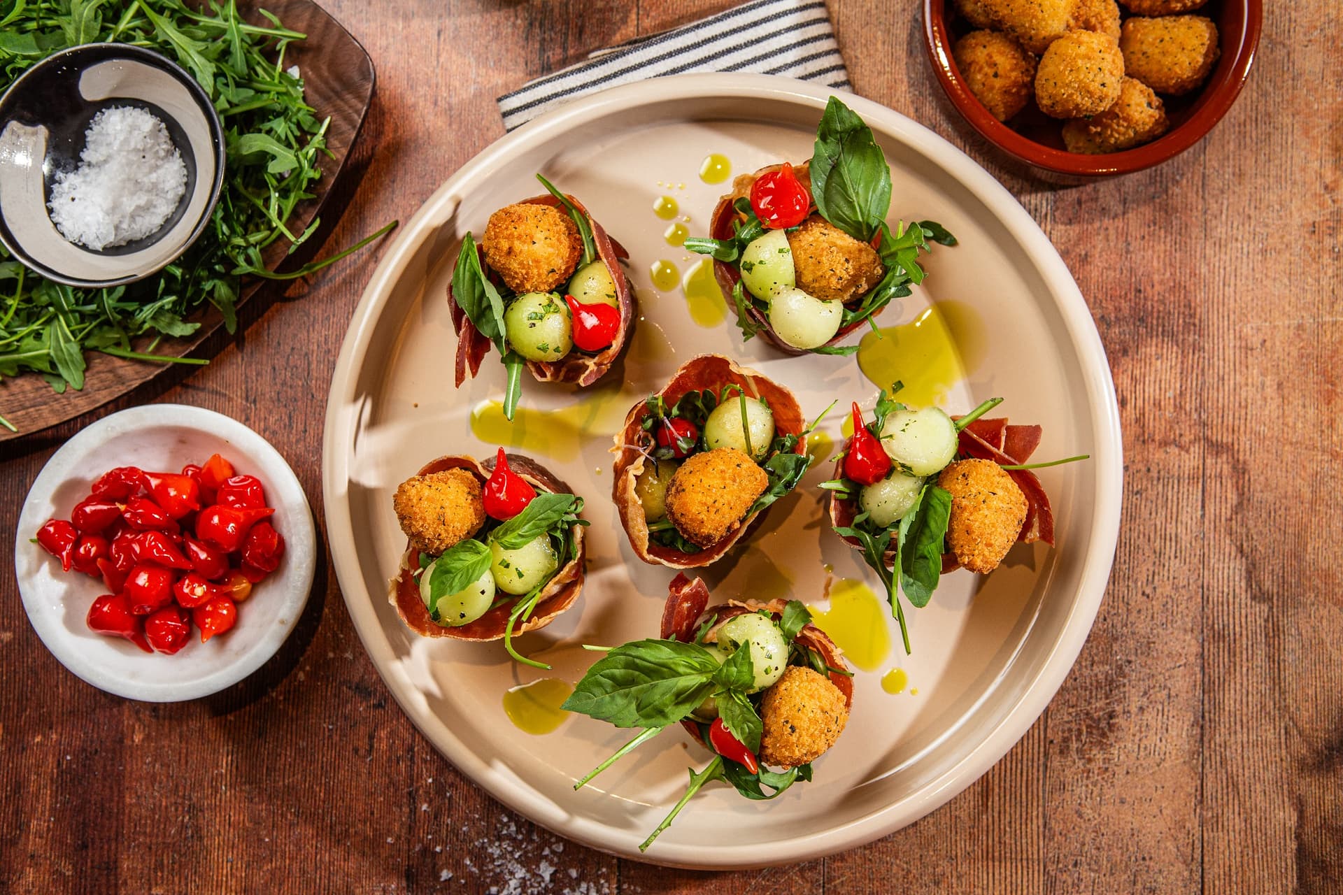 babeczki zrobione z szynki prosciutto, w środku babeczek znajdują się kulki melona, przekąski Aviko z mozzarellą i papryczki drop pepper, sześć babeczek na talerzu w restauracji