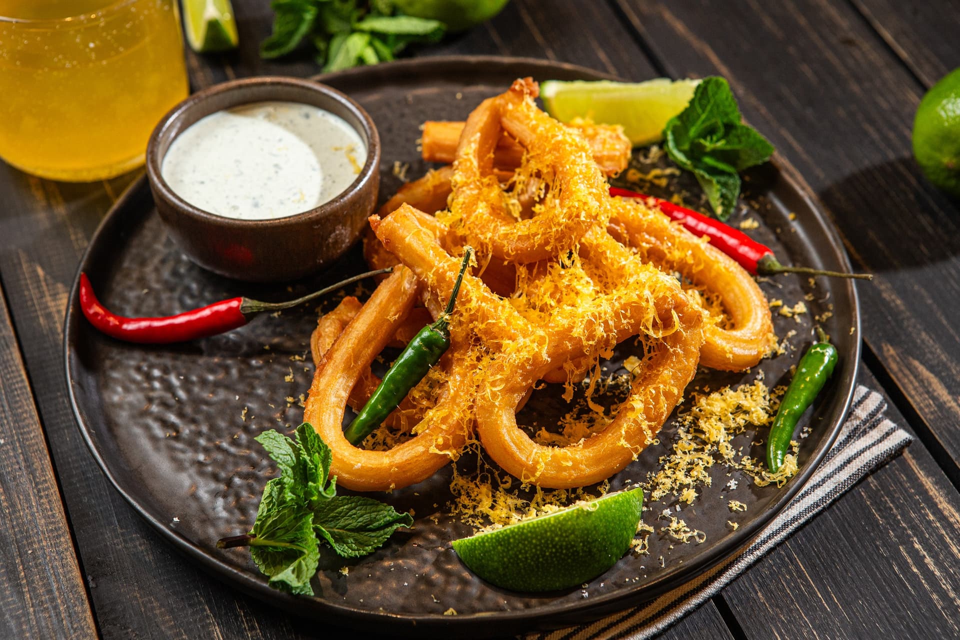 churros w kształcie pętelek od aviko posypane serem i podane na talerzu w restauracji, obok miseczka z dipem limonkowym, papryczki chili i ćwiartki limonki