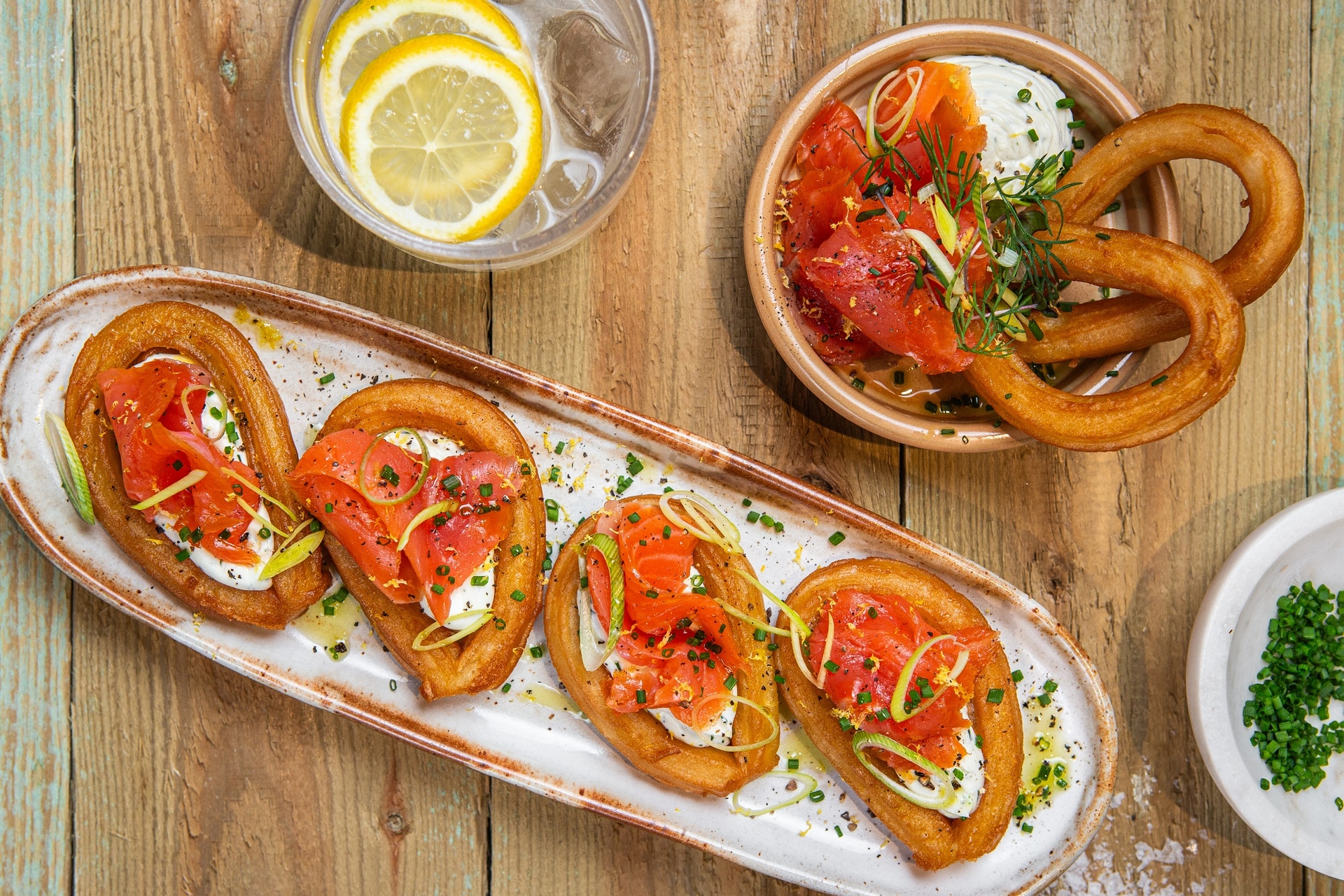 cztery churros w kształcie pętelek od Aviko zaserwowane w restauracji na podłużnym talerzyku, posmarowane pastą serową i udekorowane łososiem