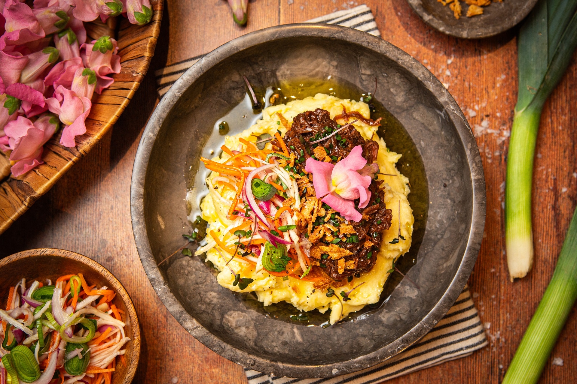 gulasz w stylu flamandzkim ułożony na talerzu na puree ziemniaczanym, obok marynowane warzywa