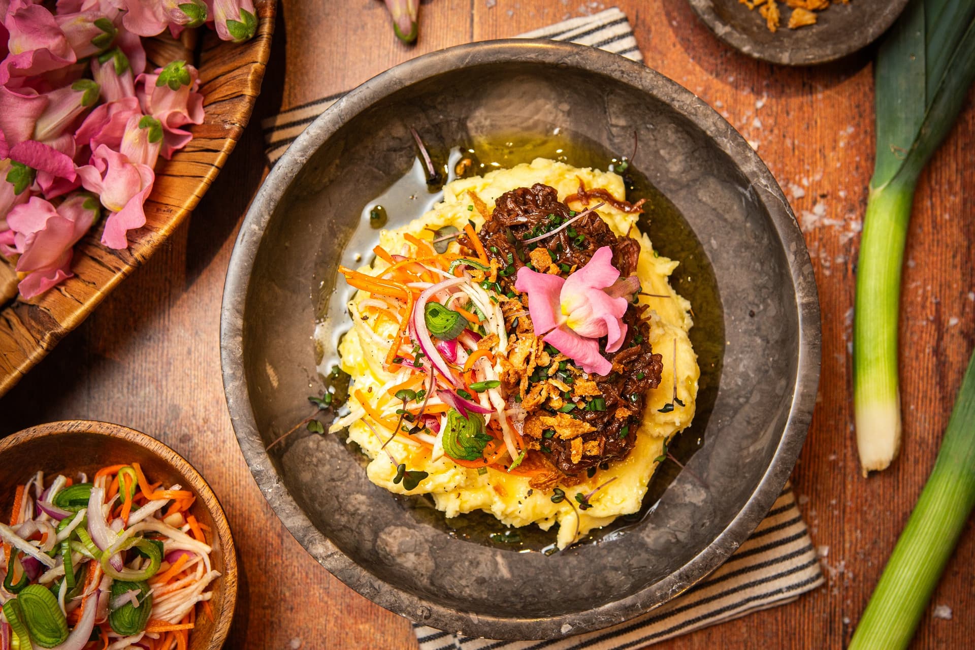 gulasz w stylu flamandzkim ułożony na talerzu na puree ziemniaczanym, obok marynowane warzywa